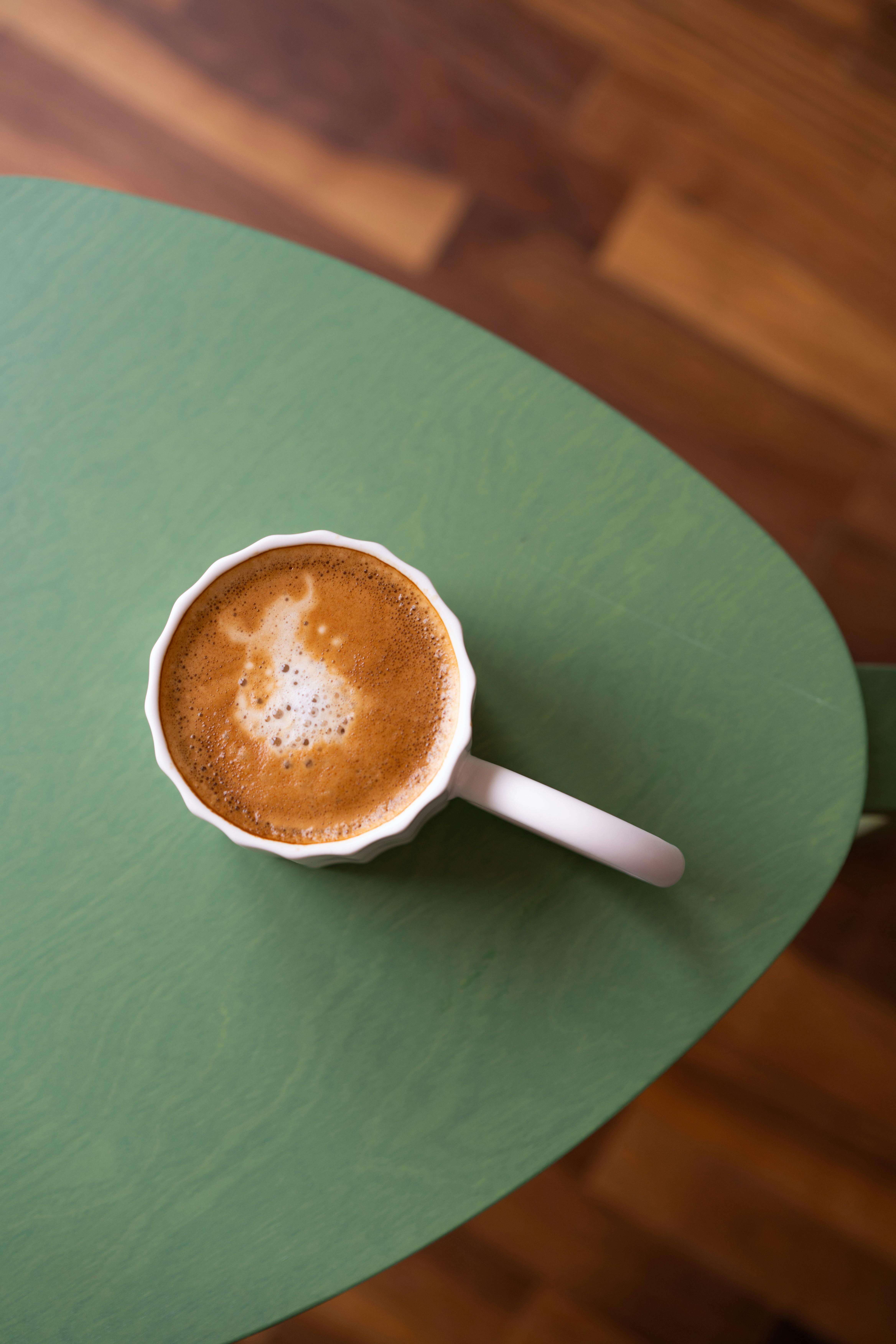 Top-down view of a cappuccino on a green table with wooden flooring background.