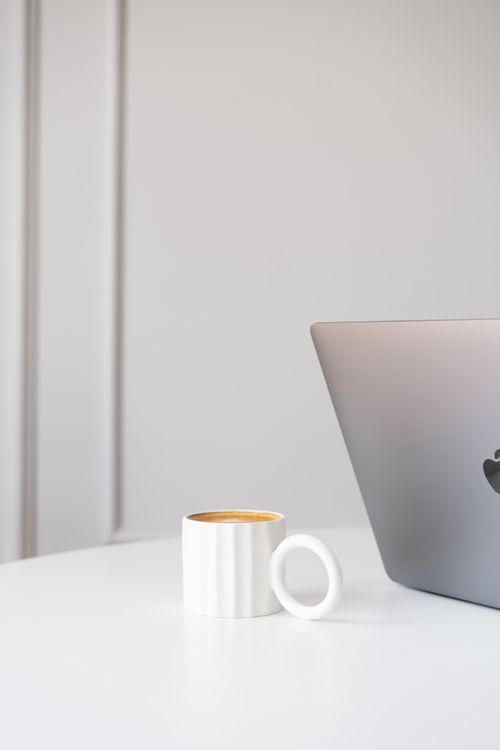 Free A modern workspace featuring a cappuccino and sleek laptop on a minimalist table with soft lighting. Stock Photo