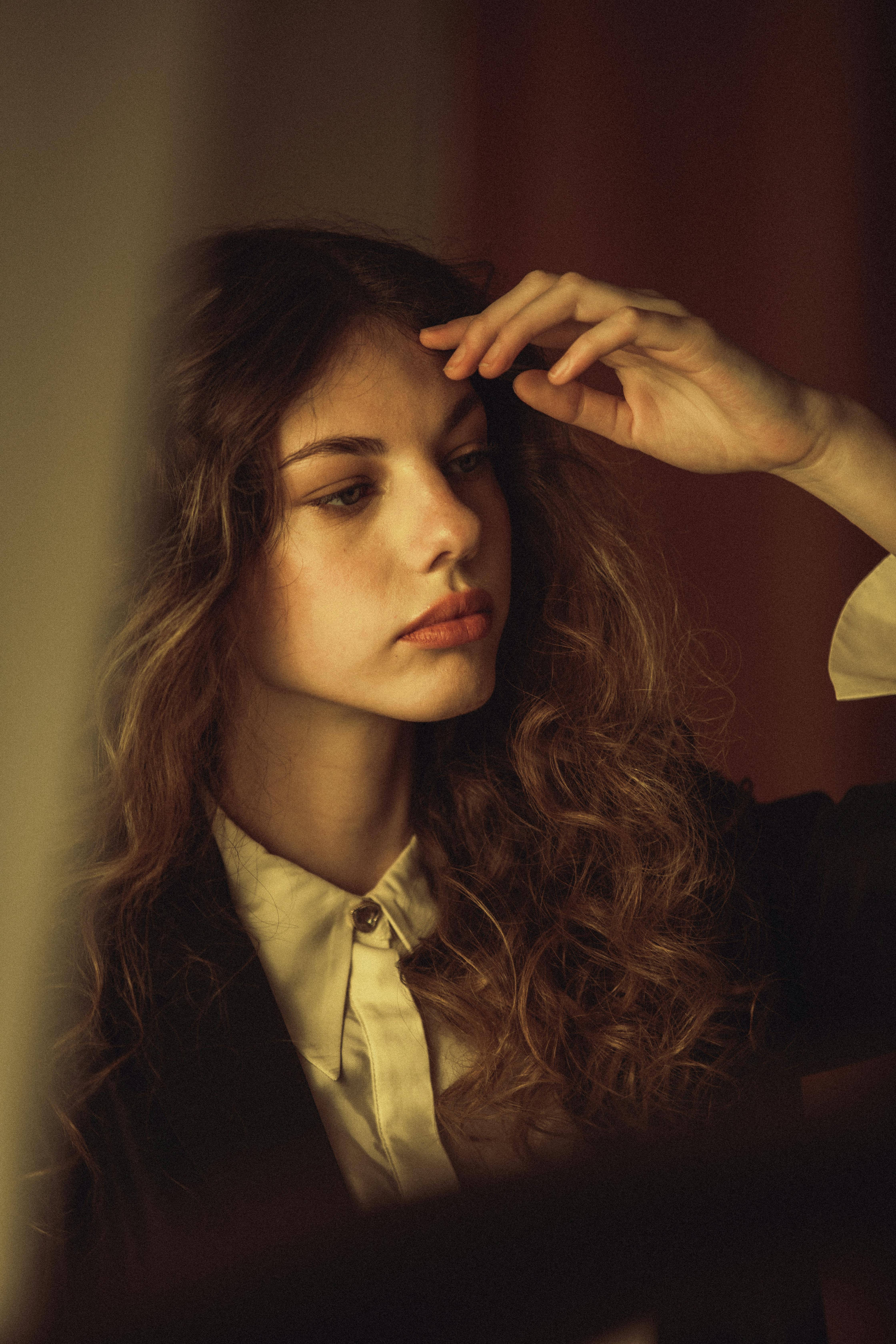 A thoughtful portrait of a woman with flowing brown hair in warm light.