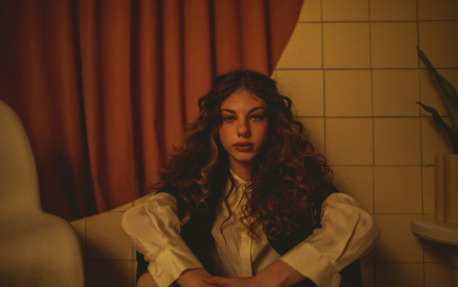Artistic portrait of a woman with curly hair sitting indoors, creating a moody, intimate atmosphere.