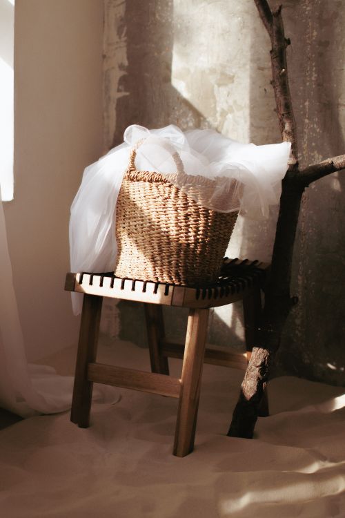 Free Wicker basket on a wooden stool with tulle draping, in a sunlit, rustic indoor setting. Stock Photo