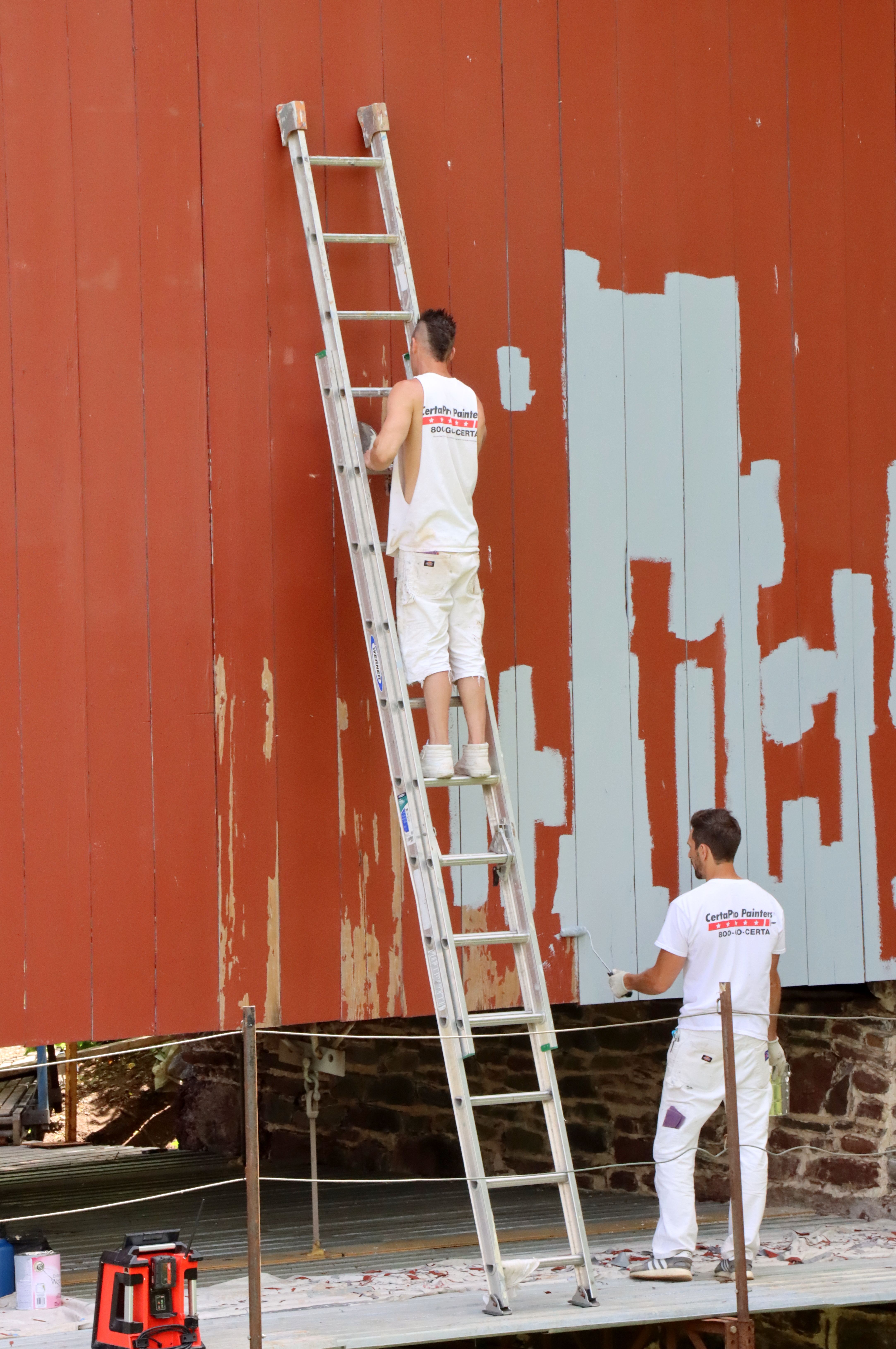 Two men repainting a large wall using a ladder, e ngaged in renovation work outdoors