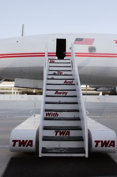 Vintage TWA airplane stairs with US flag at New York airport, showcasing retro airline travel.