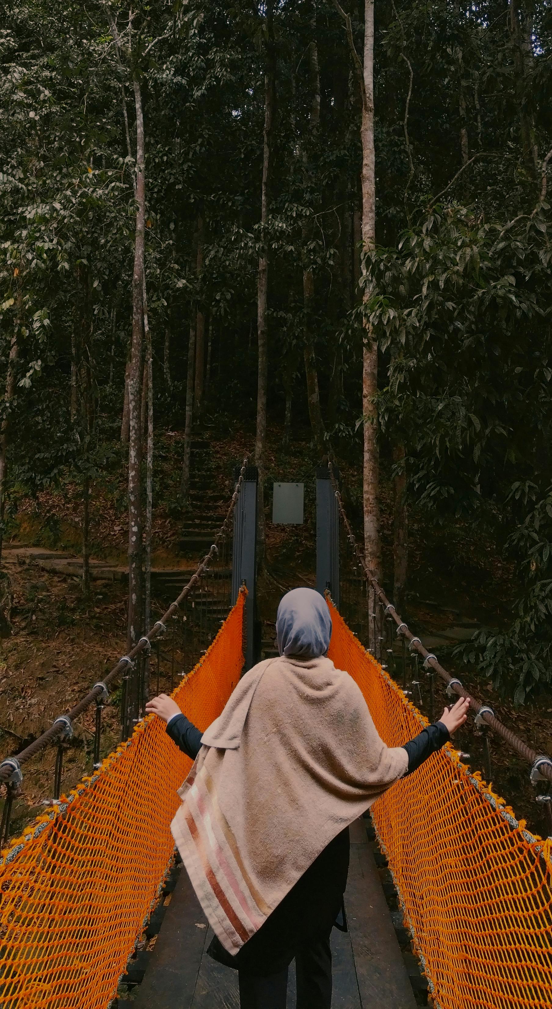 A woman in a shawl walks on a forest suspension bridge in Kuantan, Malaysia.