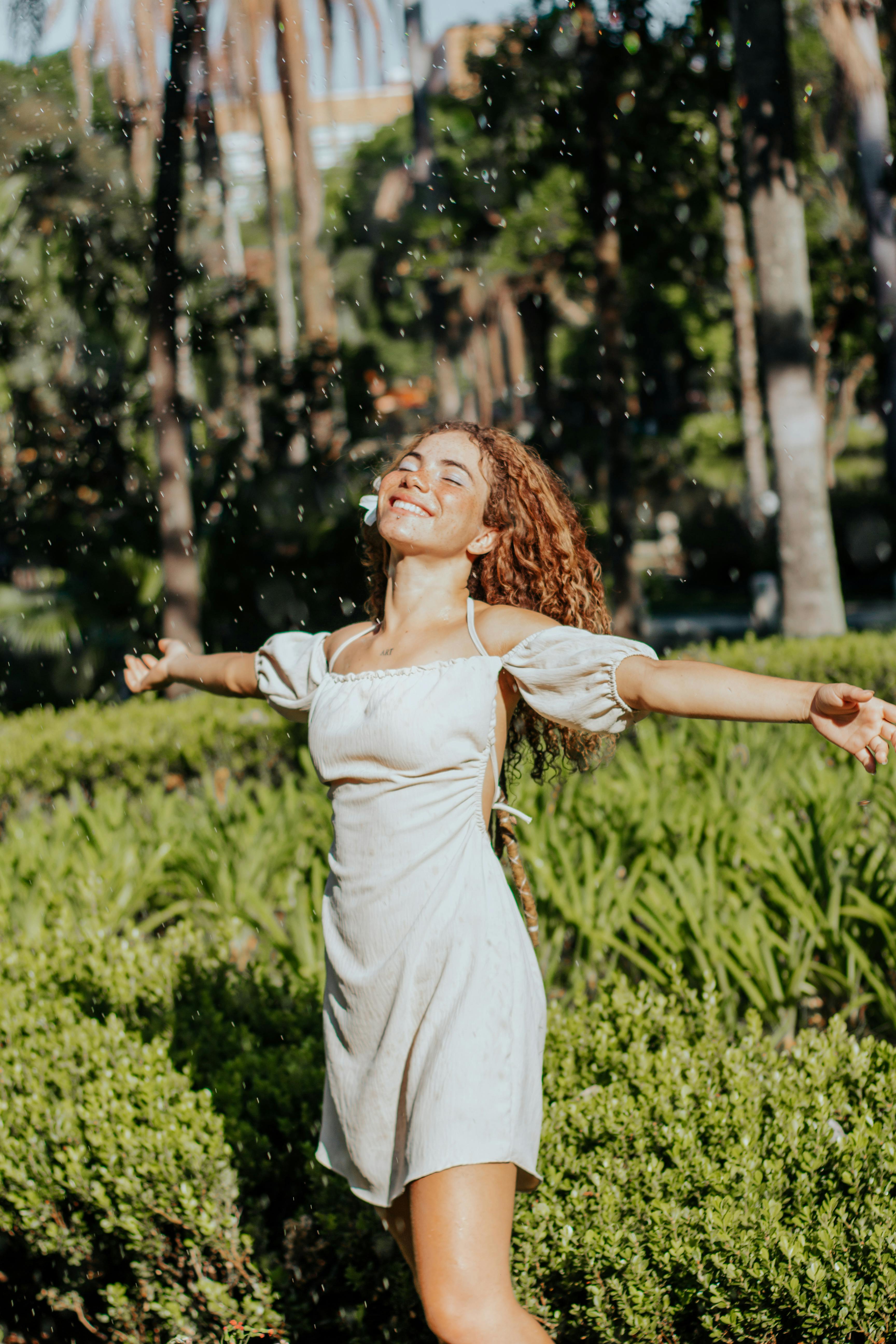 Woman in a dress enjoying a sunny day outdoors, surrounded by lush greenery.