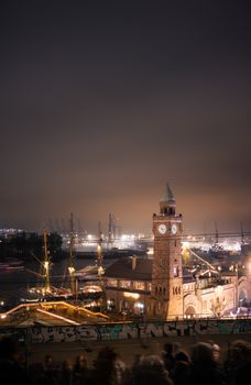 A dramatic night view of Hamburg's historic Landungsbrücken port area with illuminated ships and architecture.