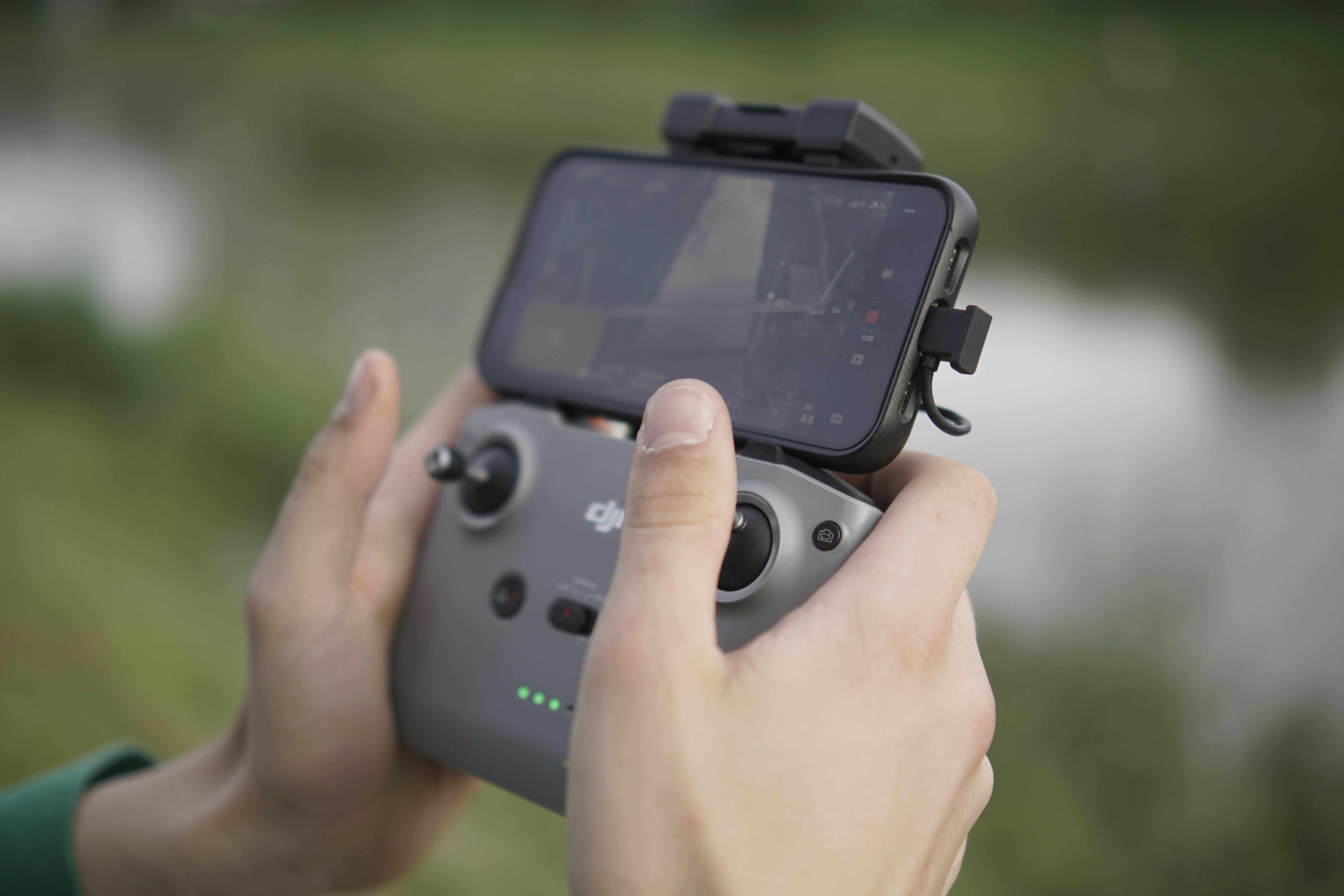 Close-up of hands holding a drone controller with smartphone outdoors, emphasizing technology and control skills.