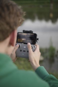 A man controls a drone using a smartphone-attached controller by a lake.