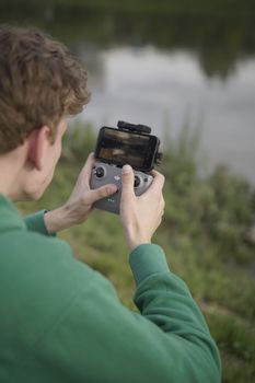 An adult man uses a drone controller near a waterbody in an outdoor setting, focused on controlling the device.