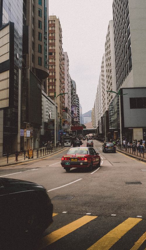 Free A lively urban street scene with high-rise buildings and traffic under a cloudy sky. Stock Photo