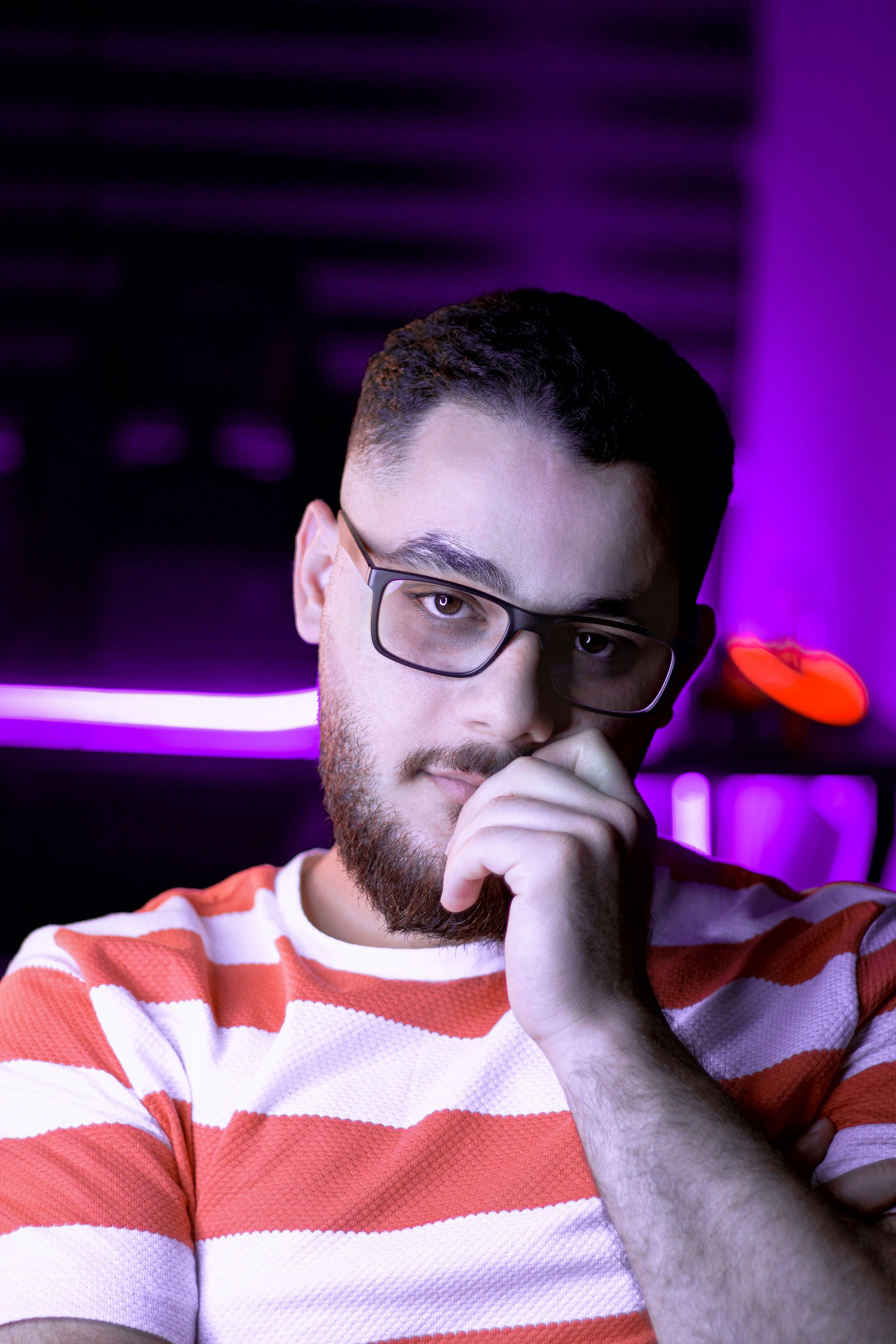 Portrait of a man in glasses, posing thoughtfully with vibrant purple lighting.