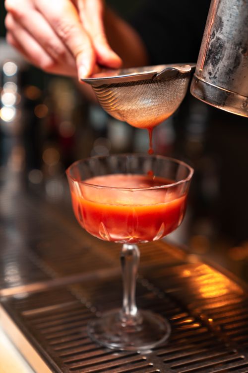 Free Close-up of a bartender straining a vibrant cocktail into a glass. Stock Photo