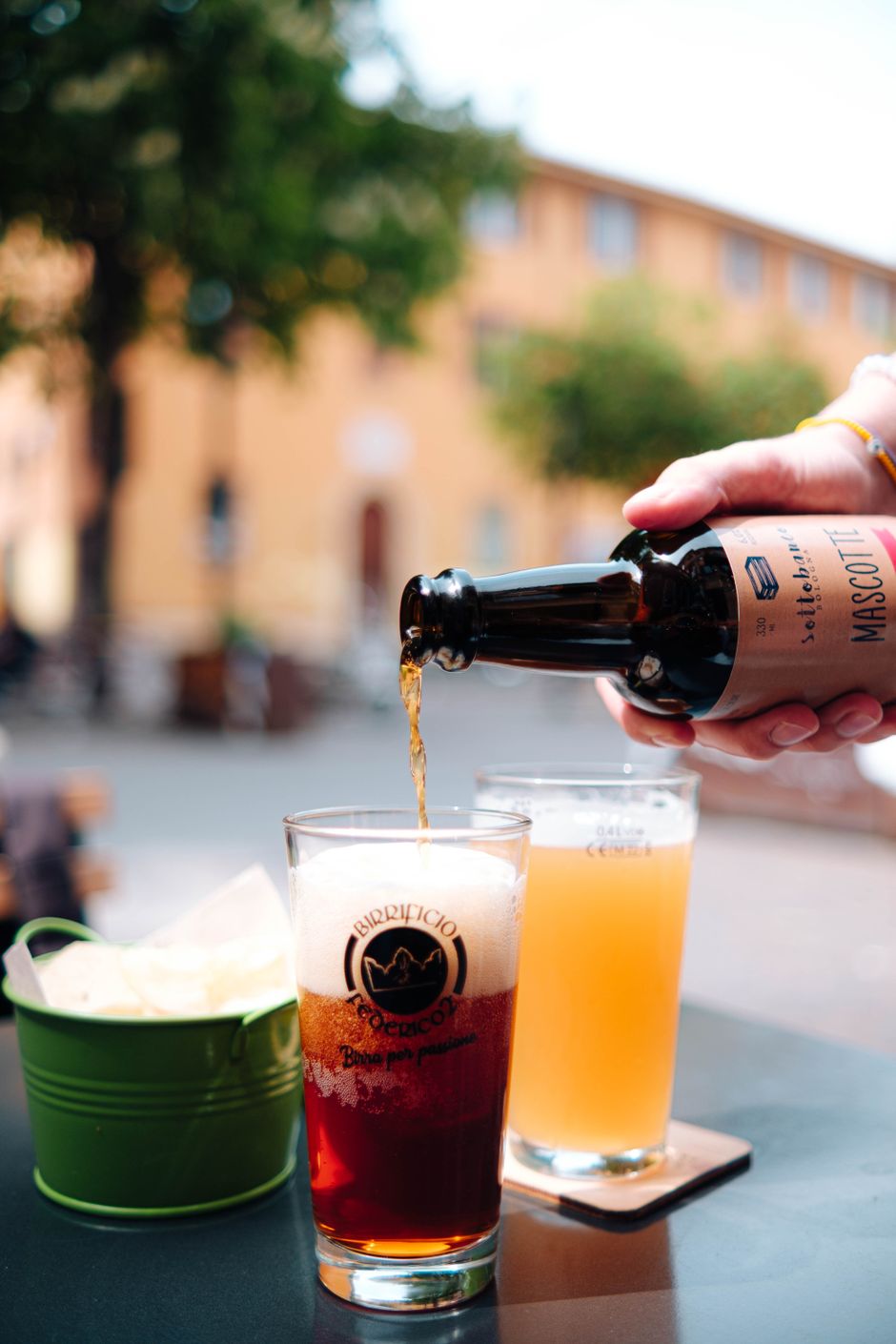 Close-up of a person pouring craft beer into a glass at an outdoor setting.