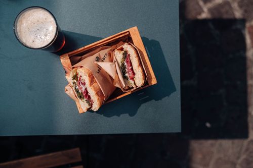 Free Delicious sandwiches in a wooden box paired with a drink on an outdoor table. Stock Photo