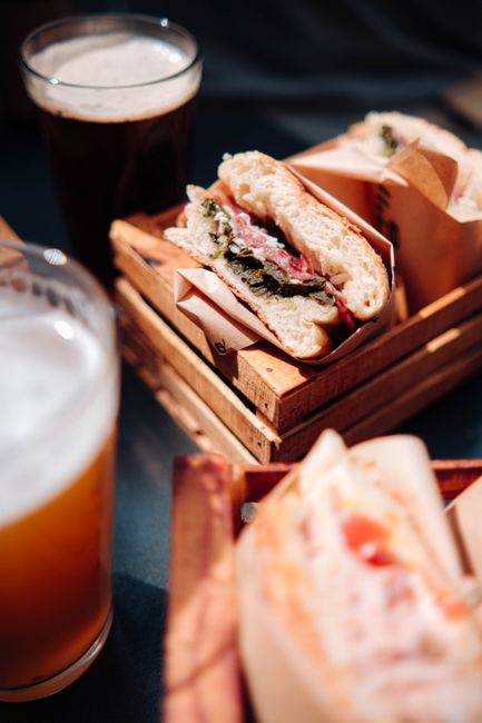 Fresh sandwiches and beer served on wooden crates with sunlight casting warm tones.