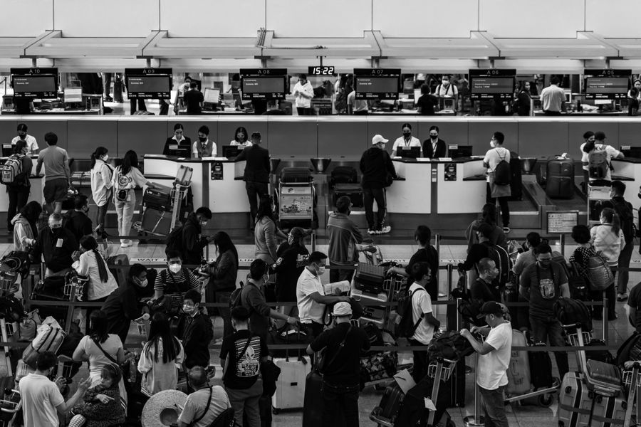 Black and white photo capturing a crowded airport check-in area filled with passengers and staff.