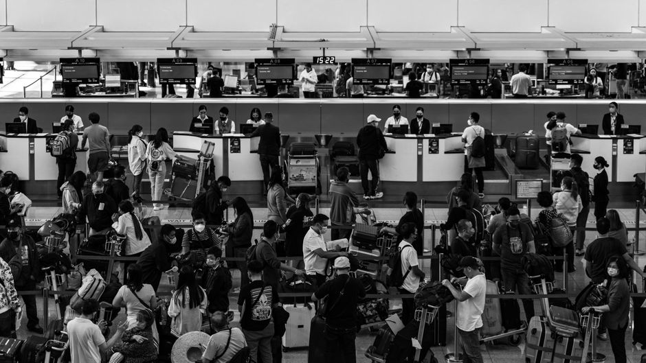 A traveller at an airport check-in counter looking at a smartphone to check airline baggage fees.