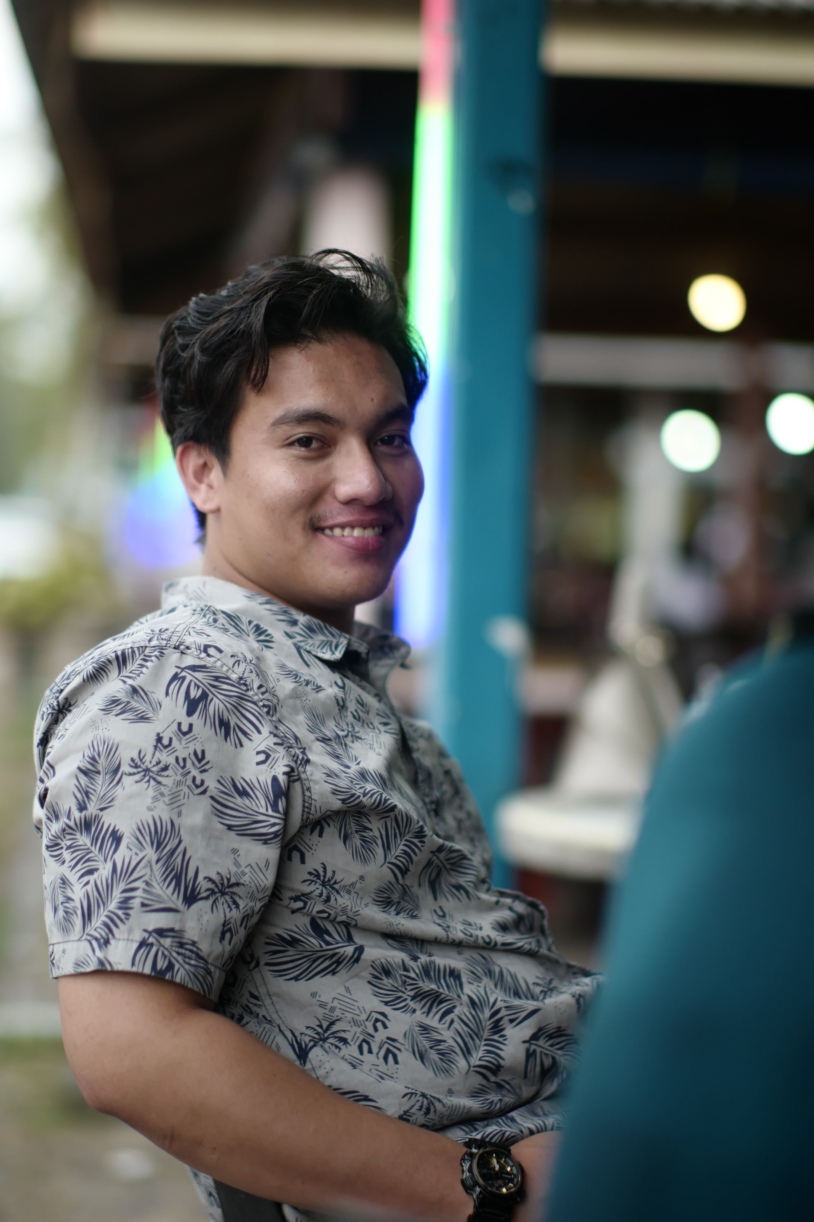 A cheerful man in a patterned shirt smiling outdoors in Kuala Dungun, Malaysia.
