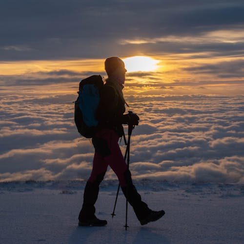 Hiker above clouds on a snowy mountain at sunrise