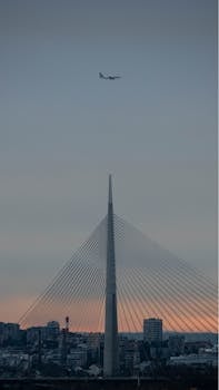 A passenger plane flying over the iconic Ada Bridge in Belgrade, Serbia during twilight.