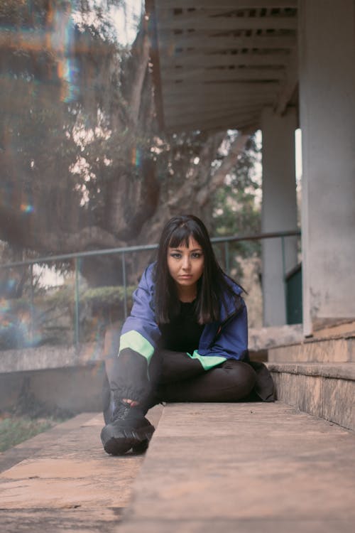 Young Woman Sitting on the Ground in front of a Building 