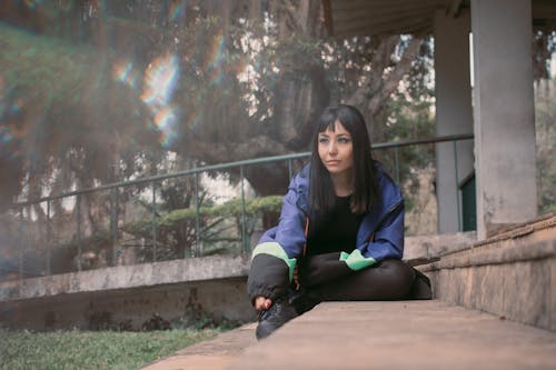 Young Brunette in a Jacket Sitting in front of a Building 