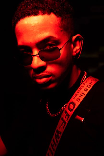 Stylish young man in cool red lighting, sunglasses, and trendy attire, captured in a vibrant nightlife setting.