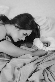 A brunette woman relaxing in bed, featuring soft lighting and monochrome tones.