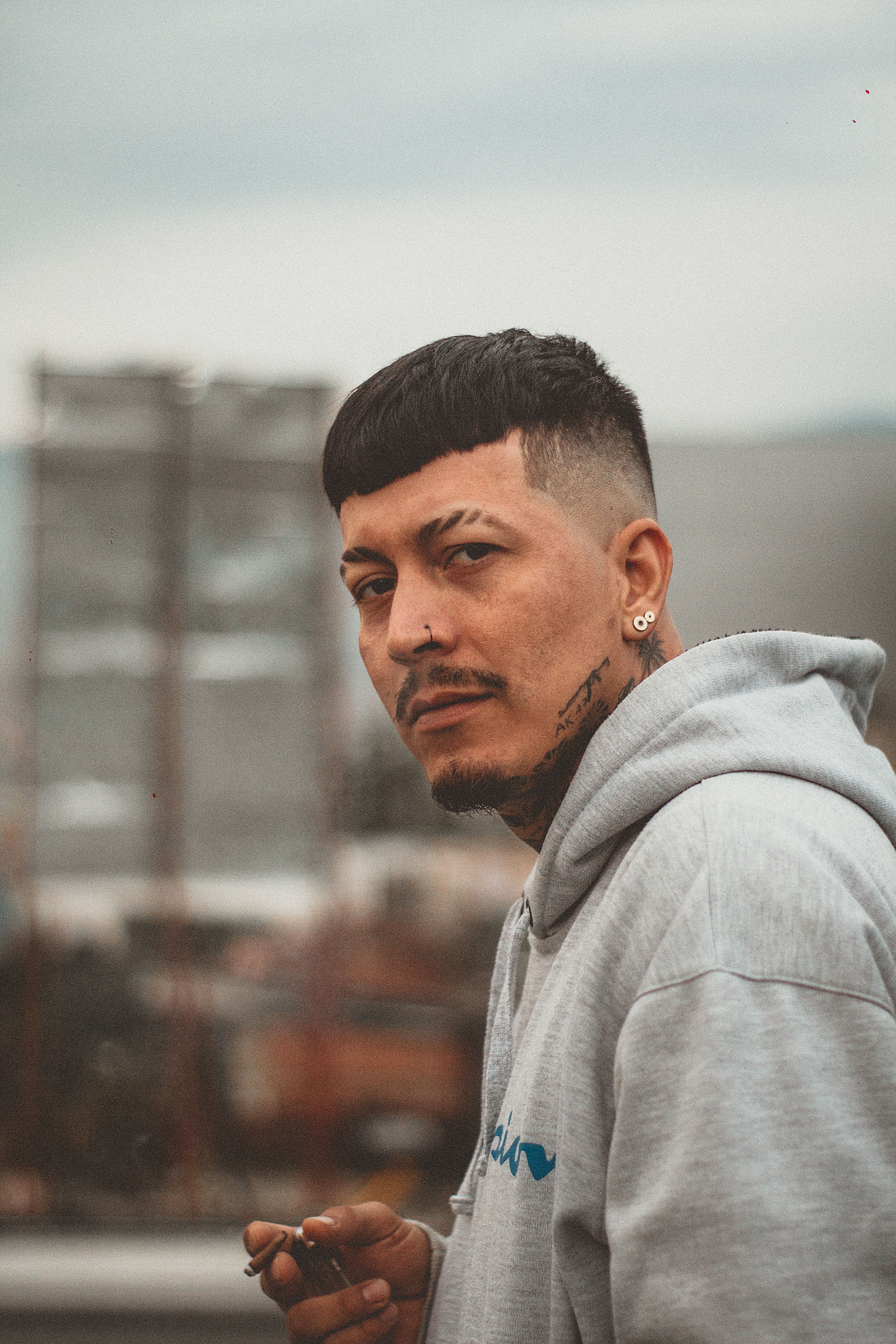 Casual urban portrait of a tattooed man wearing a hoodie, outdoors in Medellín.