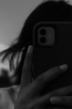 A black and white close-up of a woman holding a smartphone, capturing her reflection.