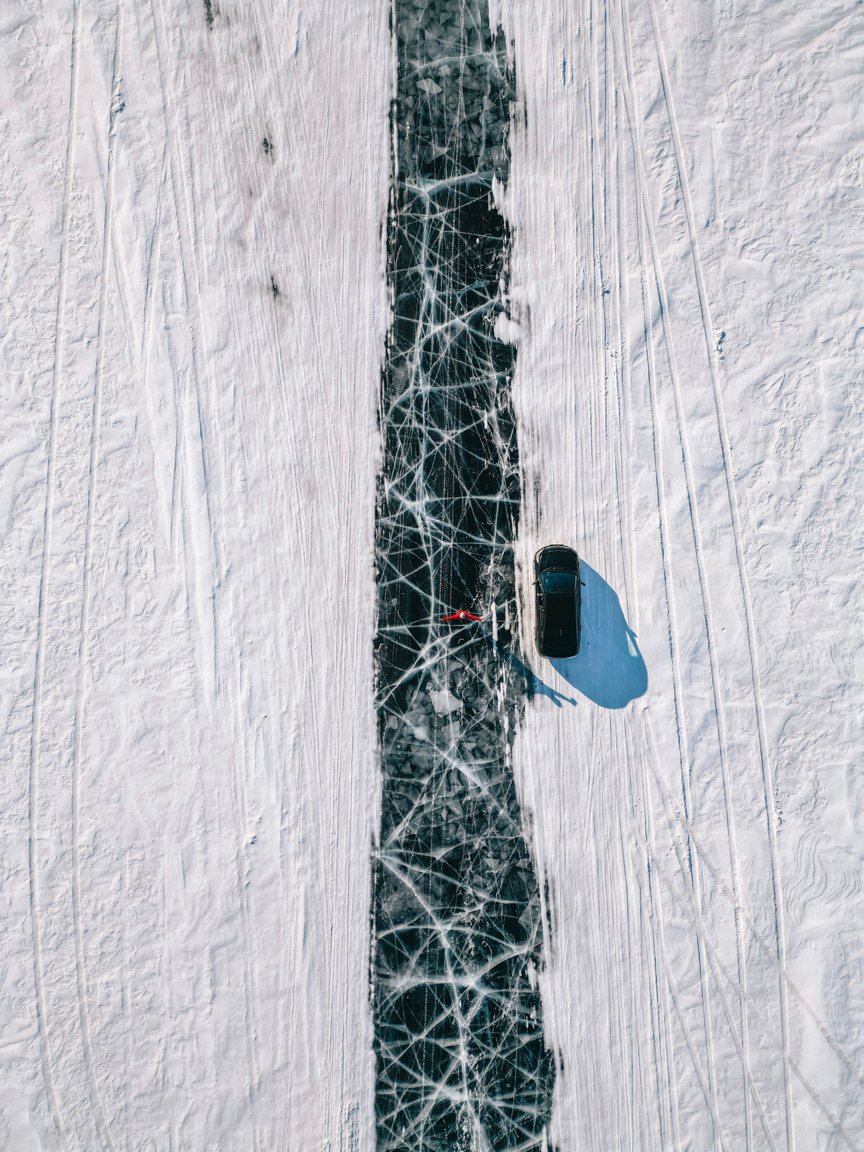A dramatic aerial shot of a car driving on the ice-covered Lake Baikal in winter, displaying unique ice patterns.