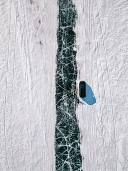 A dramatic aerial shot of a car driving on the ice-covered Lake Baikal in winter, displaying unique ice patterns.