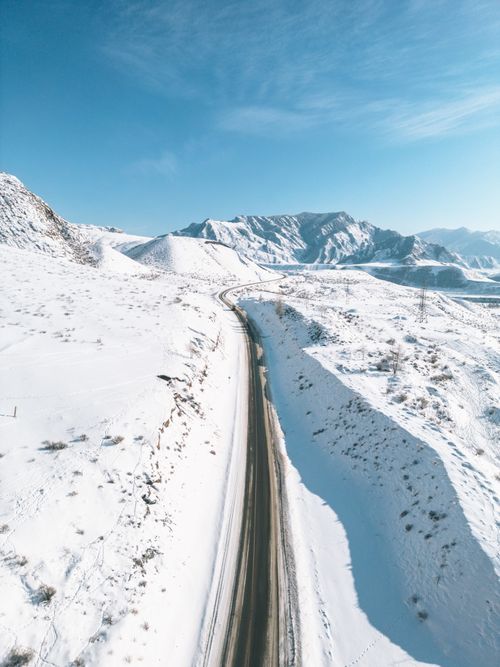 Free Drone view of snow-covered Altay mountains and winding road under clear blue skies. Stock Photo