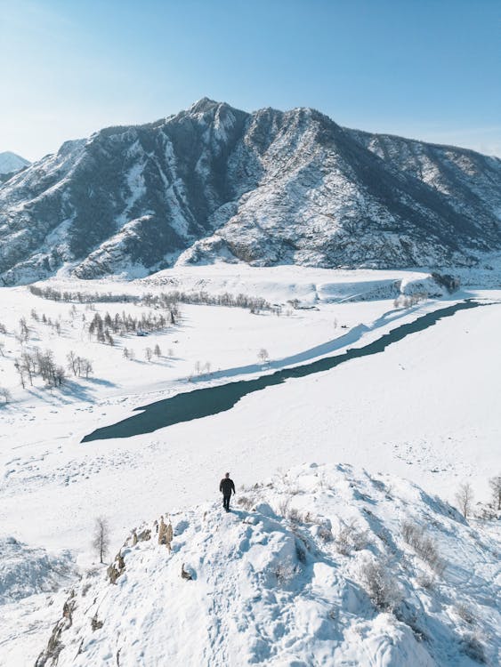 Man Standing near Lake and Hill in Winter