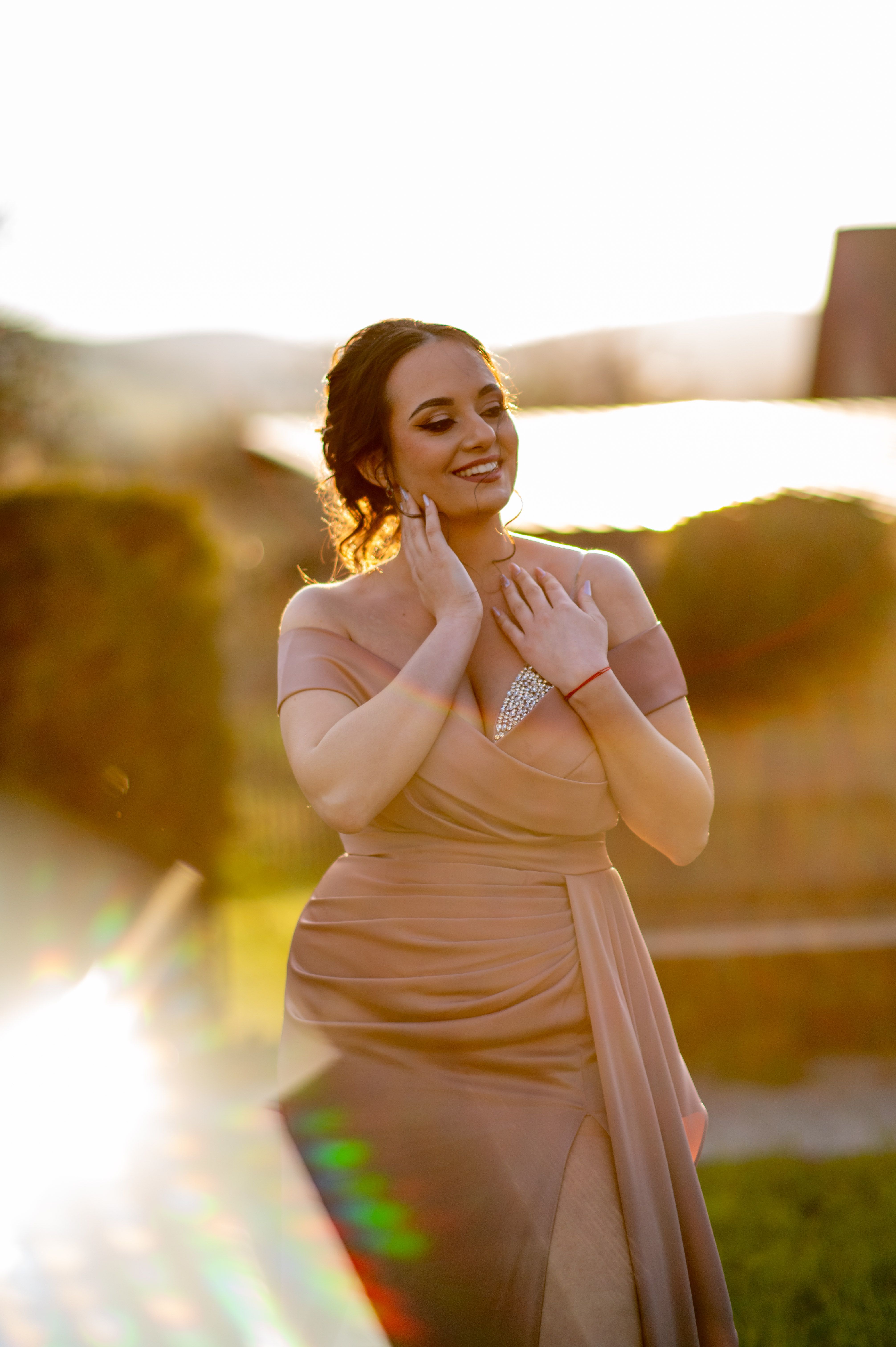 A beautiful woman in a pink dress joyfully poses outdoors during sunset in Cluj-Napoca.