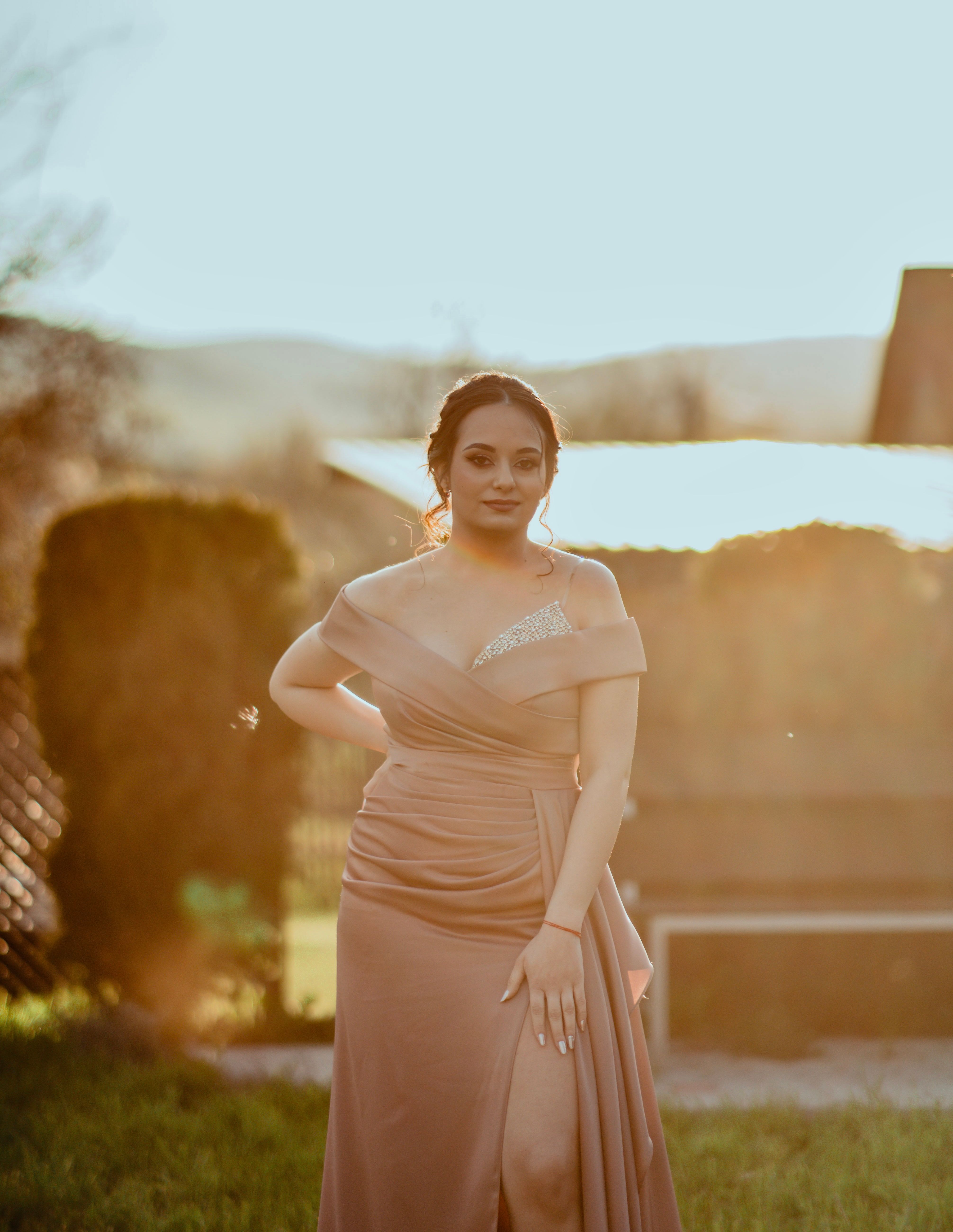 A young woman in an elegant dress posing outdoors during sunset, exuding glamour and style.