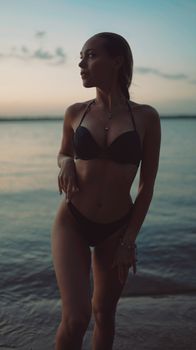 A young woman in a bikini enjoys the sunset on a serene beach.