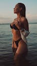 日落时分，一位身穿黑色比基尼的女子站在水中，拥抱着夏日的气息