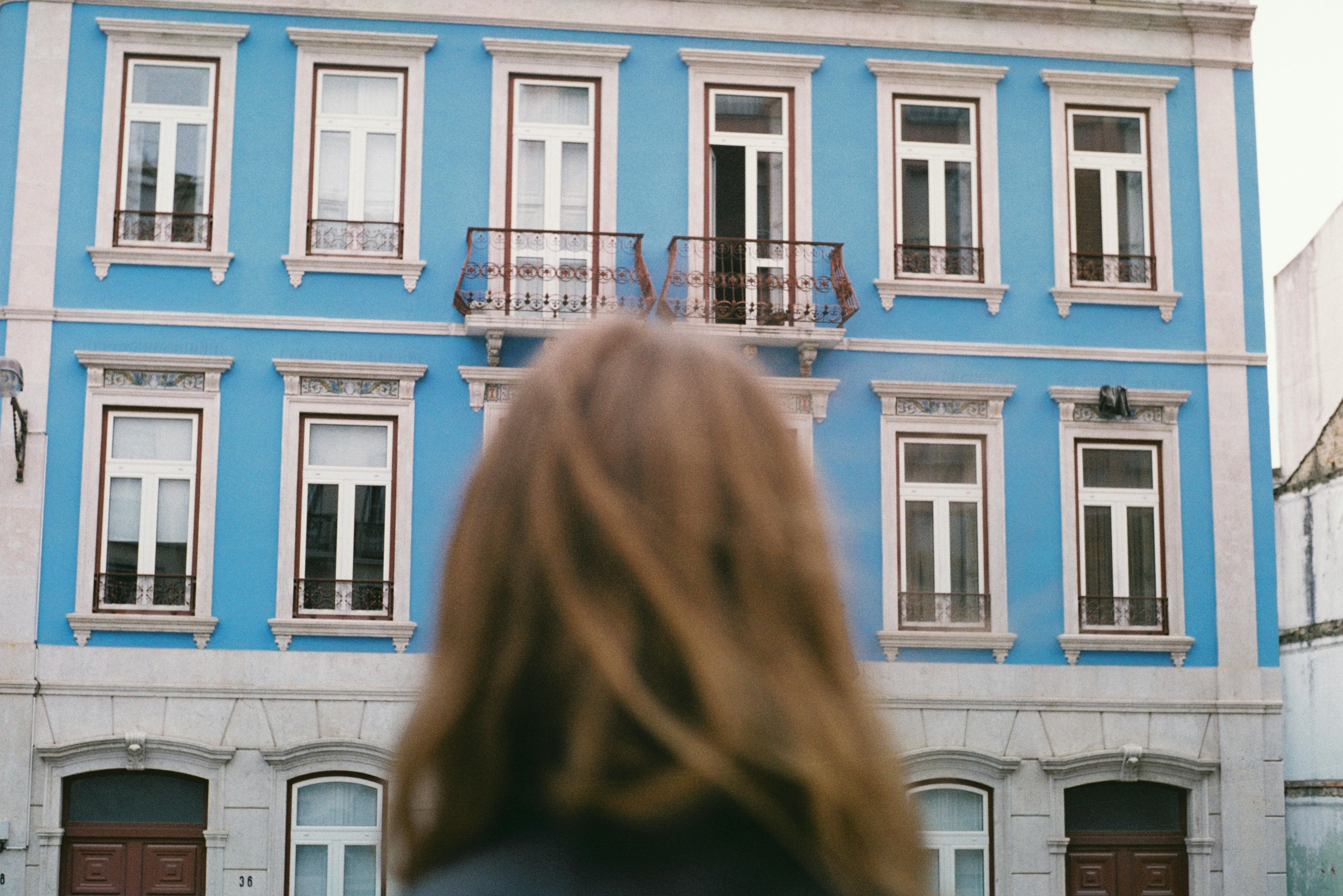 A vibrant blue building in Lisbon viewed from behind a woman.