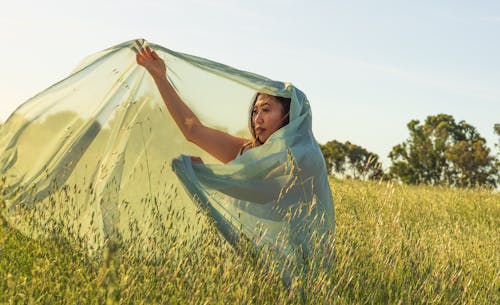 Young Woman in an Elegant Dress Posing on a Field and Holding See-through Fabric