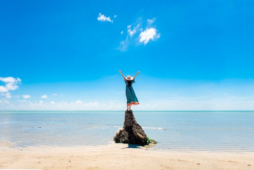 Young Woman Standing on a Rock on the Shore with Her Arms Raised 