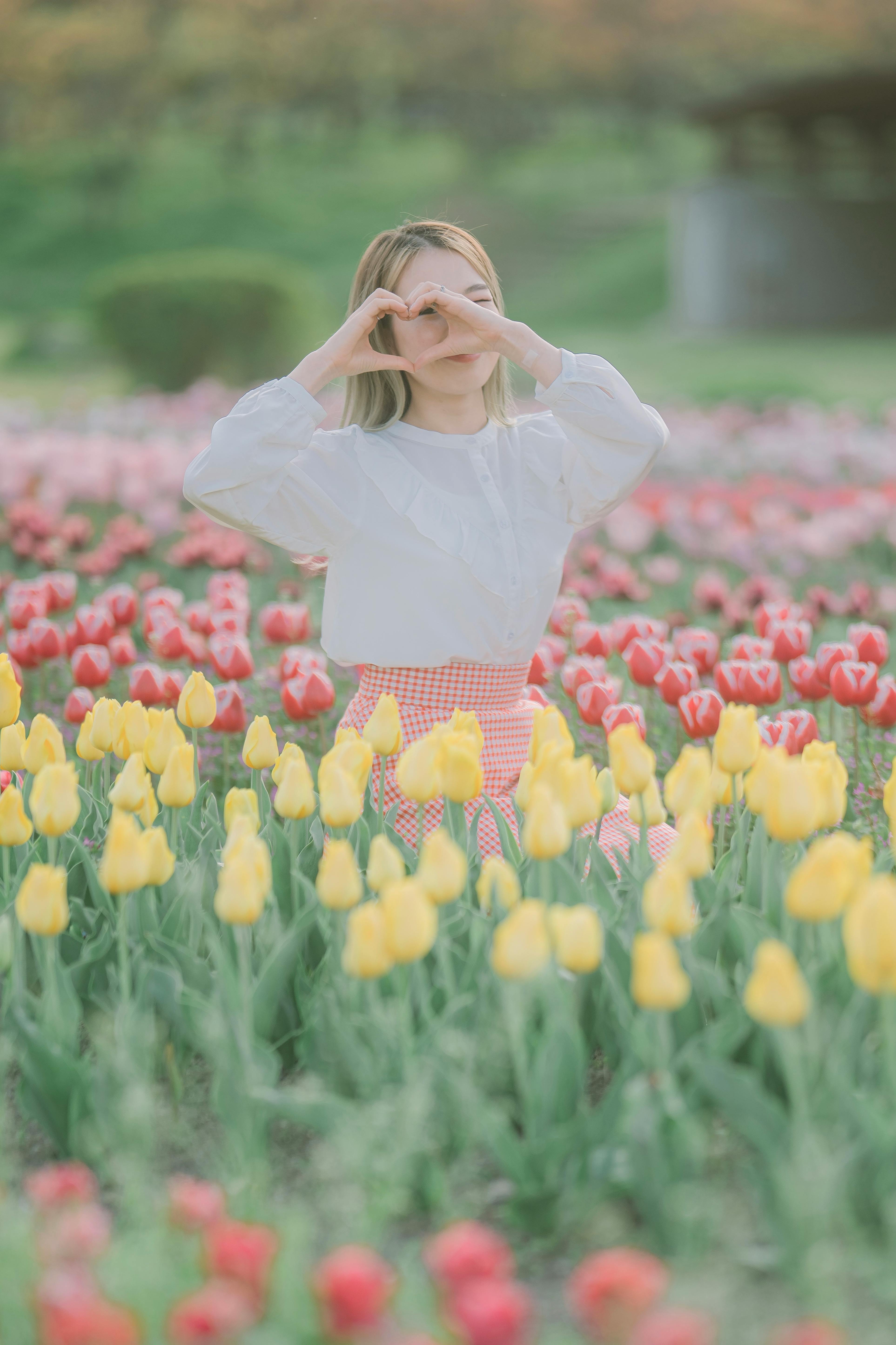 Young woman creating heart gesture with hands in a colorful tulip field during spring.