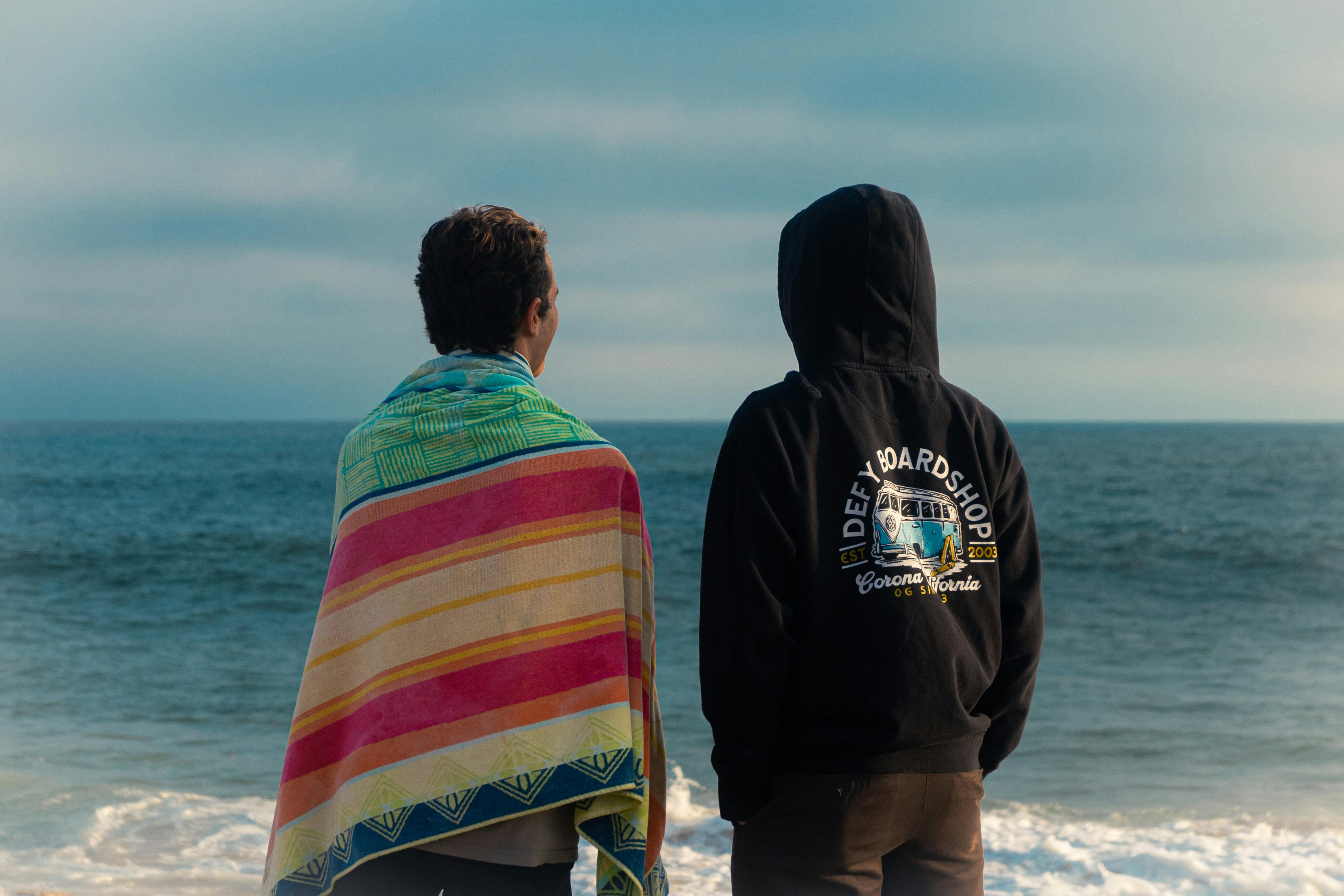 Two men stand on a beach, enjoying a relaxing moment by the sea.