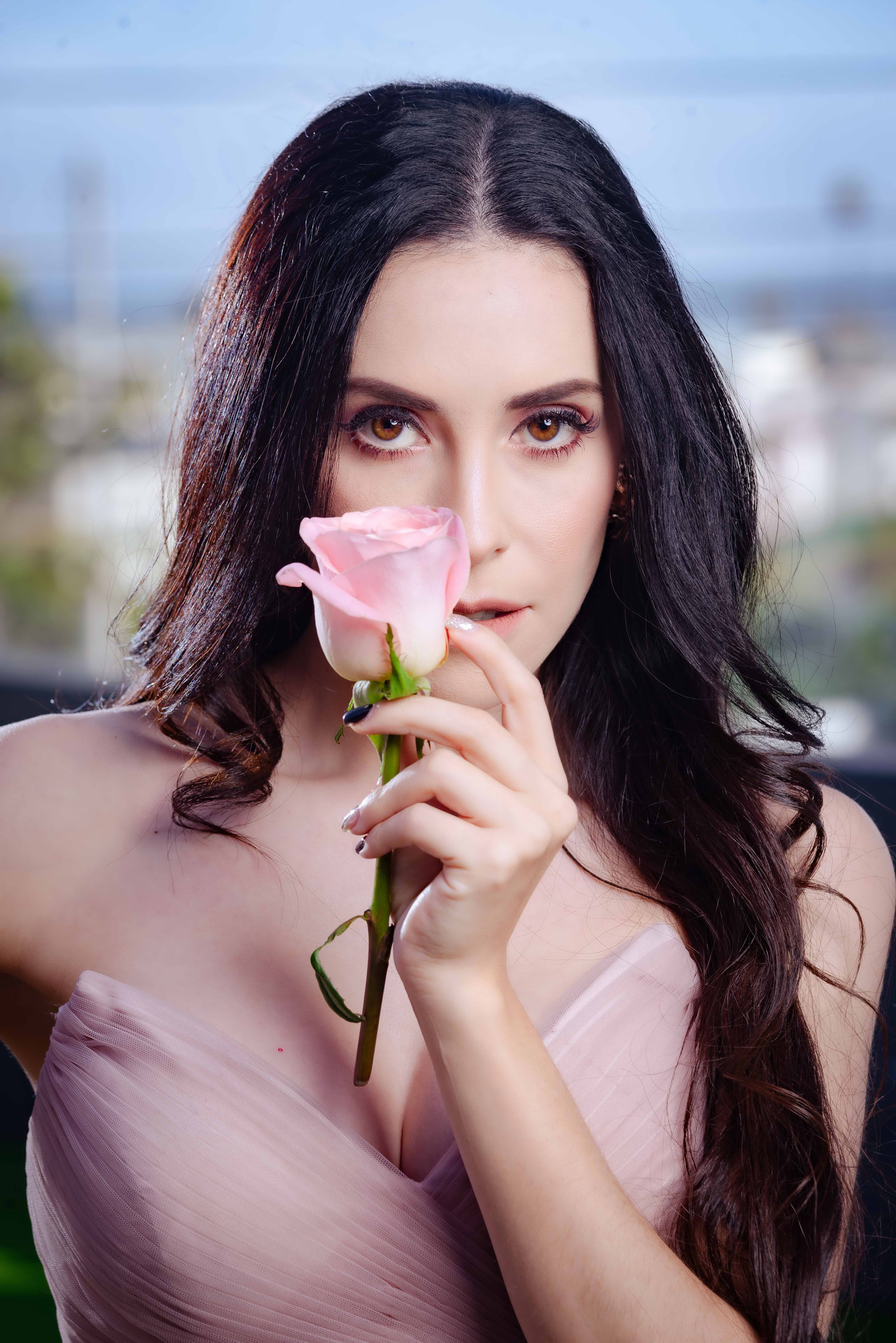 A captivating portrait of an elegant woman holding a pink rose, showcasing beauty and sophistication.