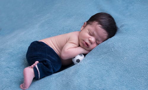 Baby Sleeping on Blue Blanket under Tiny Football