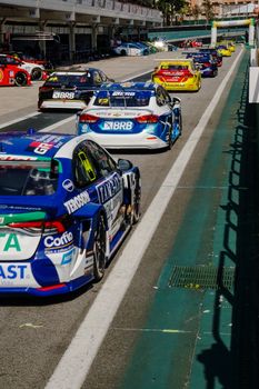 Touring cars lined up at the pit lane during a thrilling race event on a sunny day.