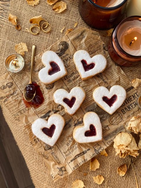 Delicious heart-shaped cookies with jam filling on a rustic burlap and paper backdrop.
