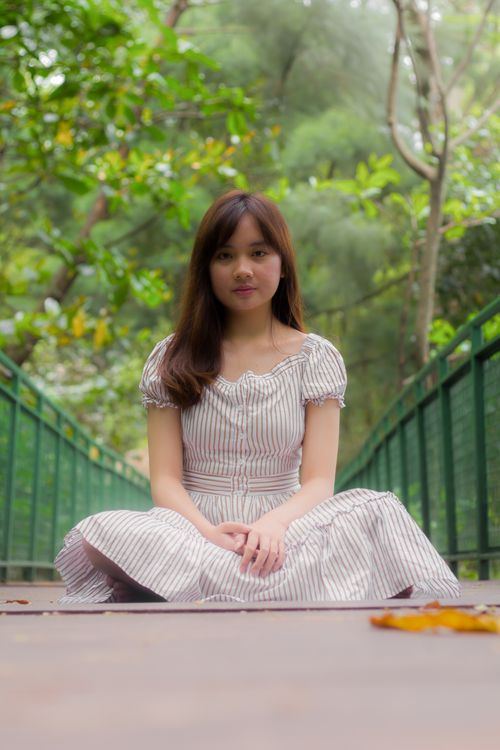 Free Portrait of a young woman in a striped dress sitting on a bridge in a lush tropical park. Stock Photo