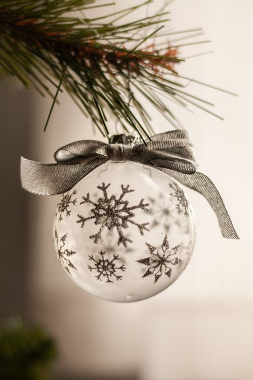 silver Christmas ornament with snowflake designs hanging from a tree branch