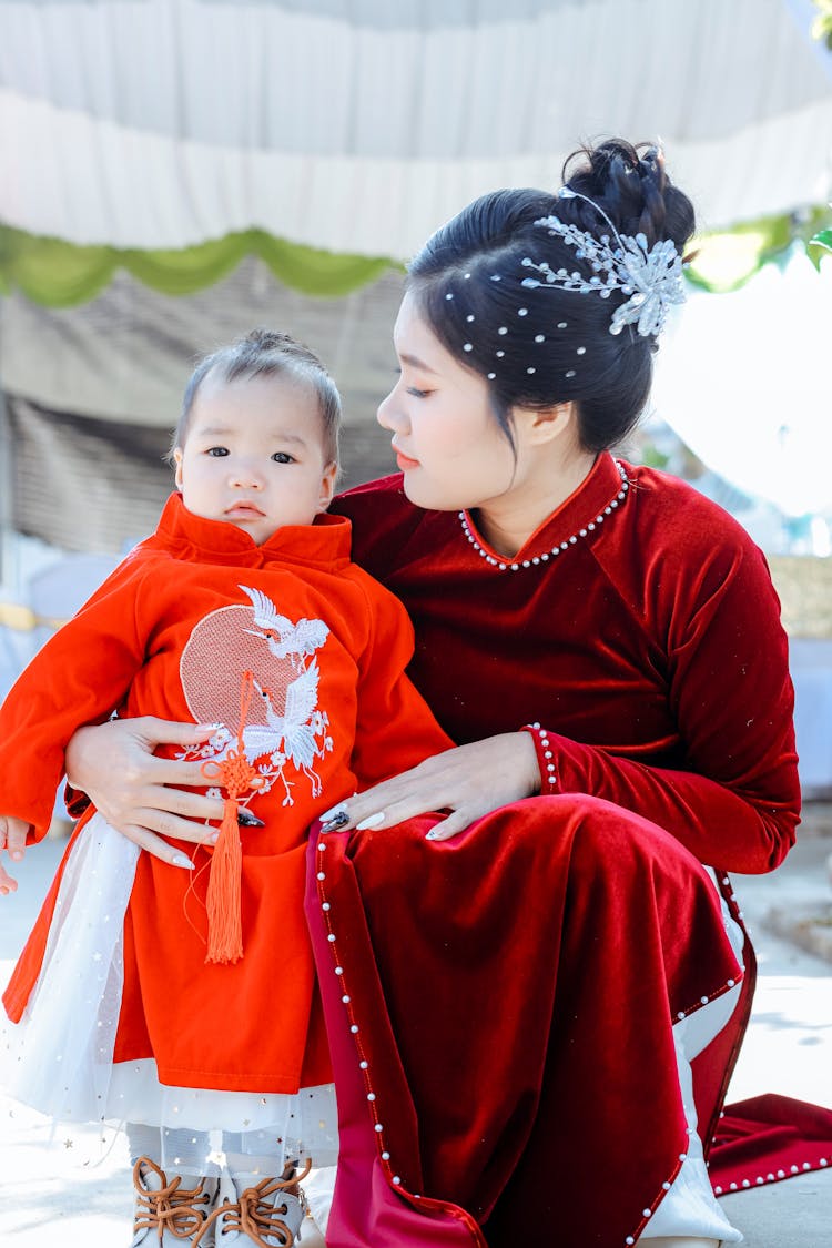 Woman Wearing Red Qipao Crouching Next To Toddler